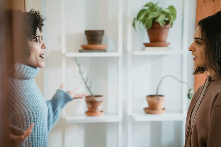 Two women engaged in conversation at home, demonstrating small behaviors that make people like you more, according to psychologists.