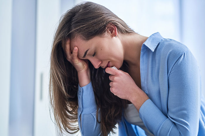 Woman in blue shirt looking distressed, holding her head, depicting regret and emotional struggle in a difficult relationship.
