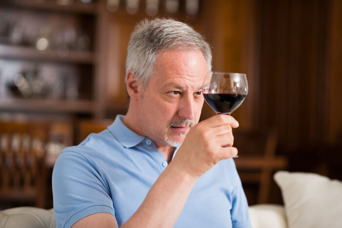Middle-aged man in blue shirt looking thoughtfully at a glass of wine, reflecting on tough reasons for staying in a relationship.