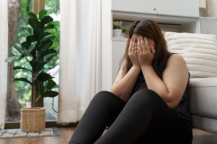 Young woman sitting on floor covering face, depicting emotional reaction to a relationship conflict with girlfriend&rsquo;s teen sister.