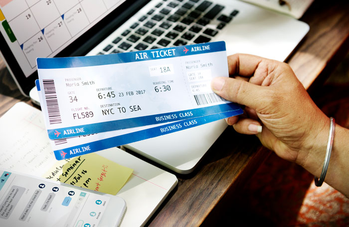 Hand holding an airline ticket near a laptop and calendar, symbolizing family stay approval without wife&rsquo;s consent.