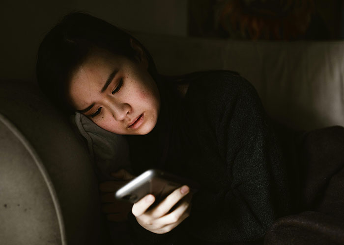 Woman lying on sofa looking at phone with concerned expression, reflecting mistress trying to contact her.