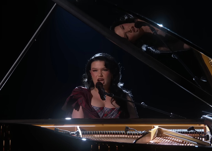 Lola Young singing at a piano on stage, with dramatic lighting highlighting her during a live music performance. Lola Young singing at a piano on stage, with dramatic lighting highlighting her during a live music performance.