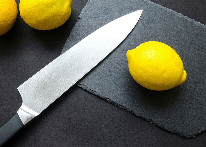 Kitchen knife next to fresh lemons on a dark slate board, illustrating unserious reasons people ended up in ER.
