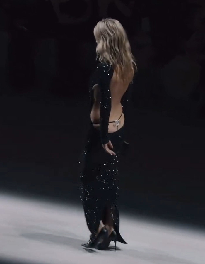 Kate Moss wearing a revealing dress with sparkling details walking the runway at a Gucci fashion show.