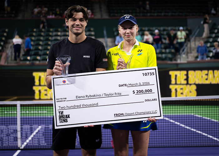Tennis star Elena Rybakina holding trophy and large check after winning Desert Champions event on tennis court.