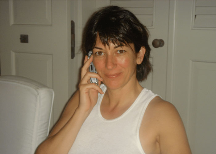 Ghislaine Maxwell on phone indoors, casual attire, highlighting prison feuds and hygiene issues in confinement setting.