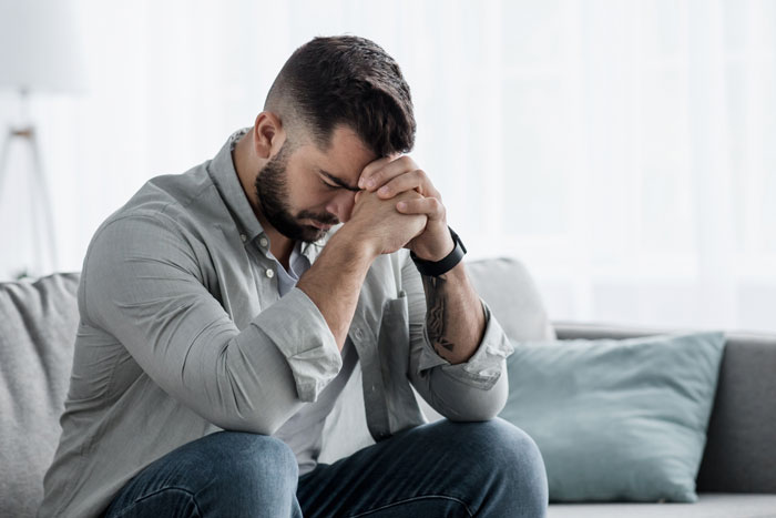 Man with beard sitting on couch looking contemplative, illustrating weird adorable and mildly concerning things relationships taught women about men