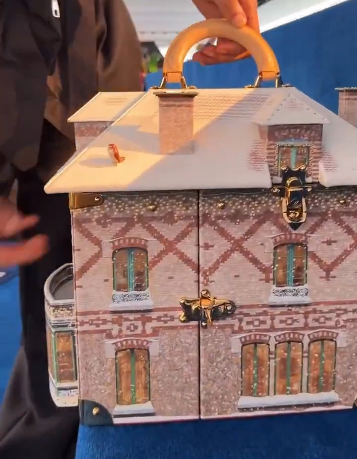 Hand holding a house-shaped bag with detailed brick and window designs, linked to Jaden Smith house bag tour controversy.