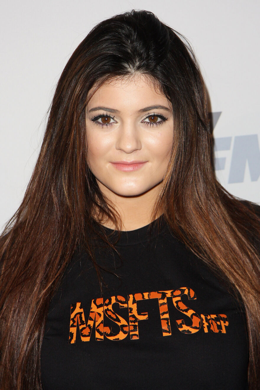 Kylie Jenner up close with natural makeup and long brown hair wearing a black shirt with orange lettering