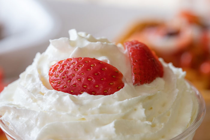 Close-up of whipped cream topped with strawberry slices, illustrating harmless secrets in relationships humorously.