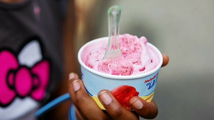 Close-up of a person holding a cup of pink ice cream with a plastic spoon.
