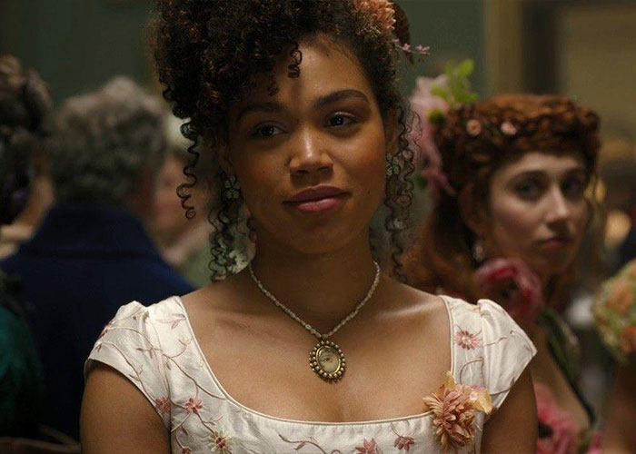 Bridgerton actress with curly hair and floral dress showing impact of mental health on her body in period setting.
