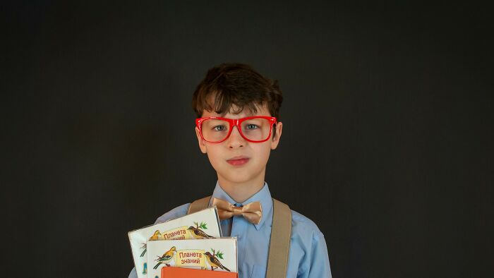 Child wearing red glasses and bow tie holding books, depicting common childhood experiences many thought were unique.
