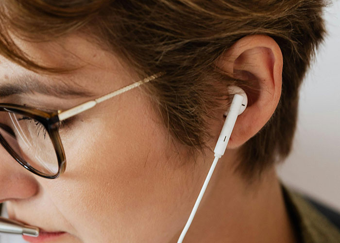 Close-up of a person wearing glasses and an earbud, listening attentively, illustrating unserious reasons people ended up in ER.