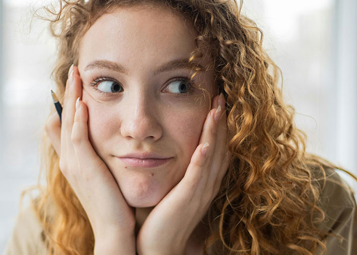 Young woman with curly hair looking sideways, appearing thoughtful about messy love triangle secrets and chaotic relationships.