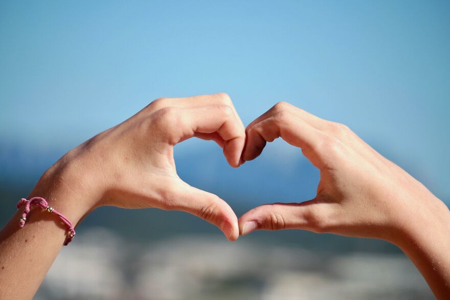 Two hands forming a heart shape against a clear sky, illustrating small behaviors that make people like you more.