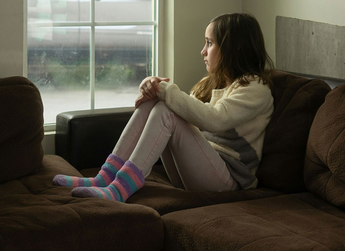 Young girl sitting alone on a couch, looking out the window with a worried expression, conveying a horrible feeling about BIL. Young girl sitting alone on a couch, looking out the window with a worried expression, conveying a horrible feeling about BIL.