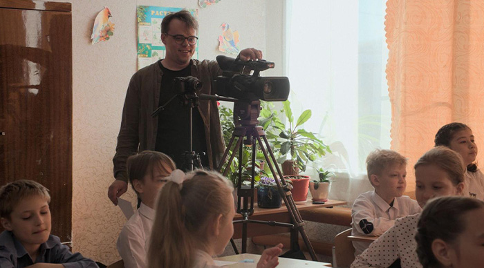 A man filming students in a classroom setting, capturing moments for community trend-based Oscar predictions.