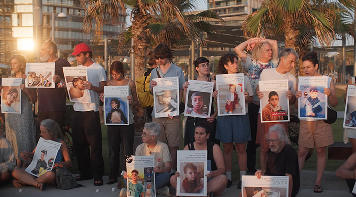 Group of people outdoors holding posters with photos, representing community trends for 2026 Oscar predictions.