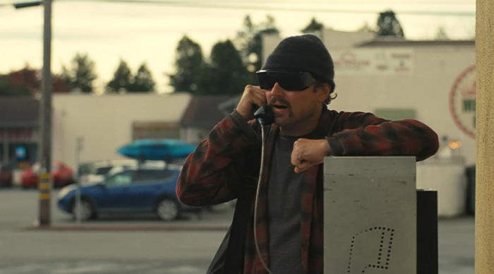 Man wearing sunglasses and a beanie using a payphone, representing 2026 Oscar predictions and community trends.