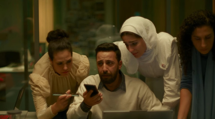 A group of four people closely examining a phone and laptop, representing community trends for Oscar predictions.