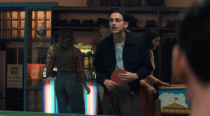 Young man holding ping pong paddle in a retro game room scene related to Oscar predictions and community trends in 2026.