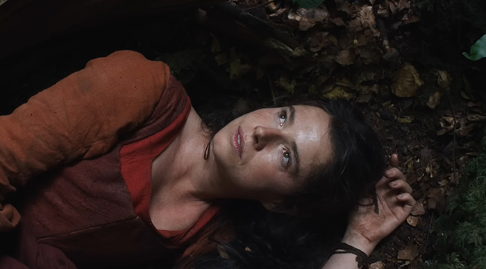 Woman in rustic clothing lying on forest floor, evoking themes for 2026 Oscar predictions and community trends.