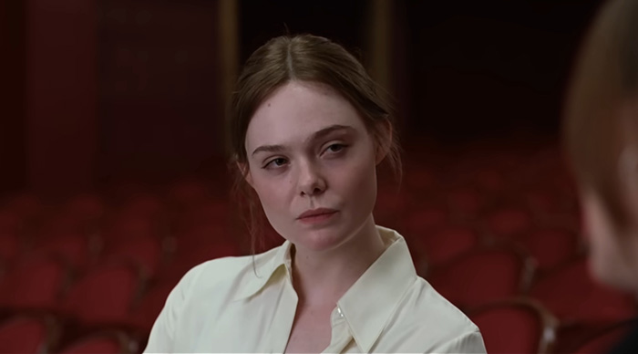 Young woman in white shirt sitting in empty theater, reflecting on 2026 Oscar predictions based on community trends.