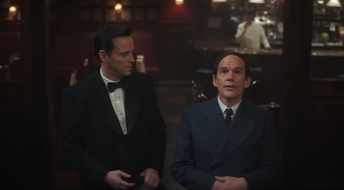 Two men in formal suits sitting in a dimly lit bar scene related to 2026 Oscar predictions and community trends.