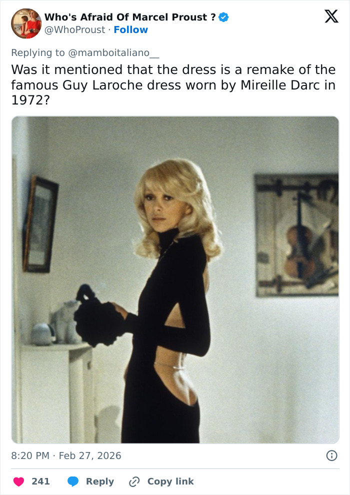 Blonde woman wearing a revealing black dress reminiscent of Kate Moss&rsquo; Gucci show outfit, posing indoors in vintage style.