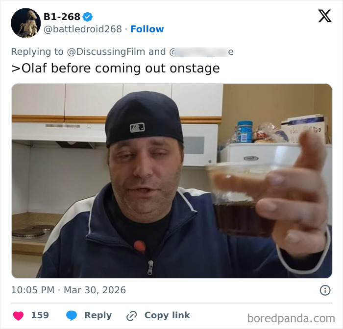 Man wearing a baseball cap holding a drink, humorously representing Disney's animatronic Olaf before collapsing.