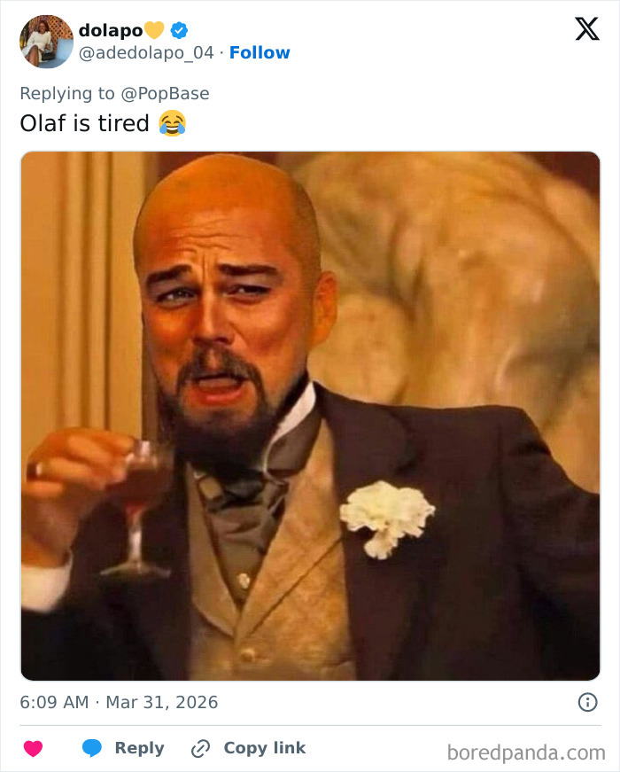 Man in vintage suit laughing and holding a drink, reacting humorously to Disney's animatronic Olaf collapse.