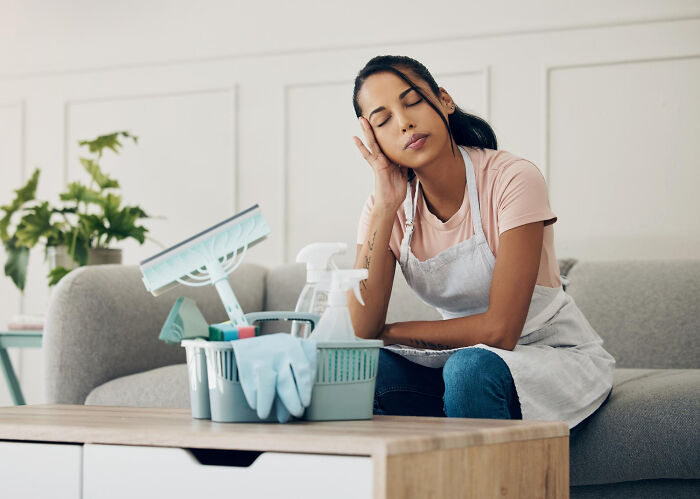 Woman looking tired sitting on a couch with cleaning supplies, highlighting common struggles women thought were normal.