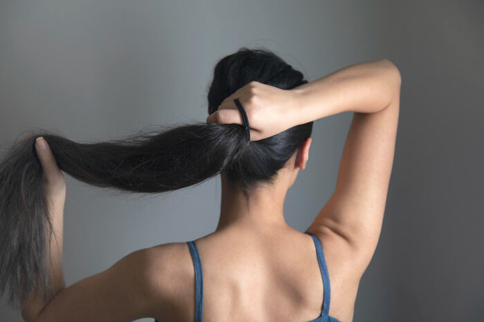 Woman with long hair tying ponytail, representing secrets women don't tell men about period wardrobe and support.