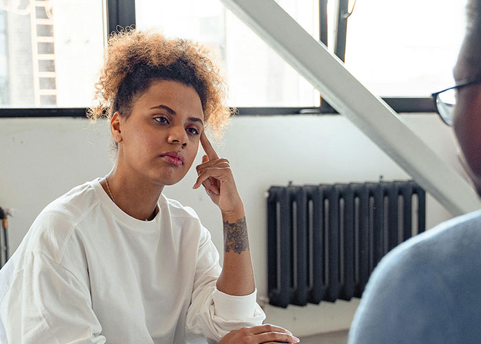 Woman in a white shirt thoughtfully listening while discussing relationship issues about being happily divorced indoors.