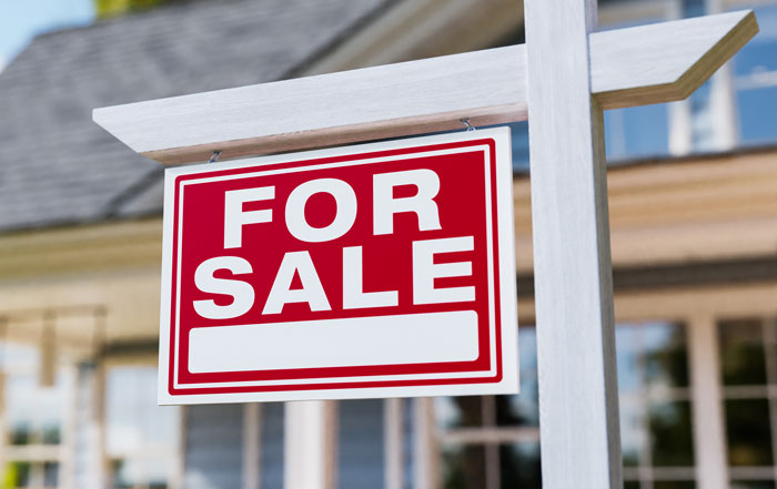 Red and white for sale sign hanging outside a house, symbolizing confusion about coworkers knowing personal information.