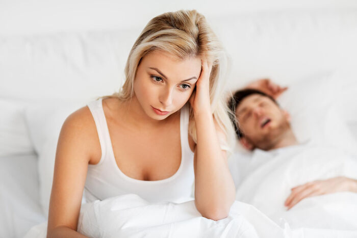 Woman looking worried in bed while partner sleeps, representing common misconceptions about being a woman.