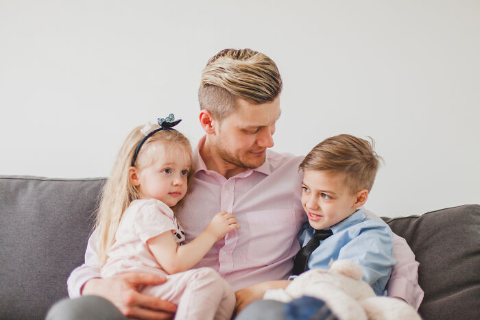 Man sitting on a couch holding two children, reflecting on tough reasons for staying in a relationship despite challenges.