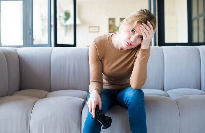 Woman looking frustrated on a couch holding a game controller, highlighting common challenges women face daily.