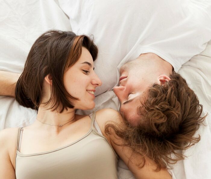 A couple lying in bed smiling at each other, illustrating intimate moments and women's secrets not told to men.