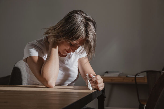 Woman sitting at a table looking distressed, reflecting on tough reasons for staying in a relationship despite hating partner.
