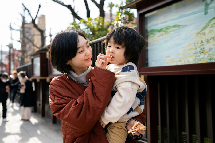Young woman holding a child while feeding him a snack, illustrating tough reasons for staying in a relationship despite challenges.