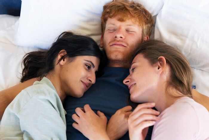 Three people lying close together on a bed, showing comfort and connection among women and support.