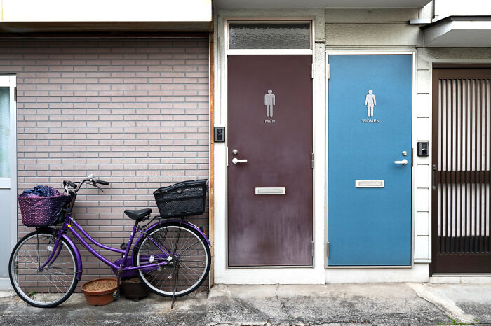 Bizarre culture shock with men and women restroom doors side by side and a purple bicycle parked outside.