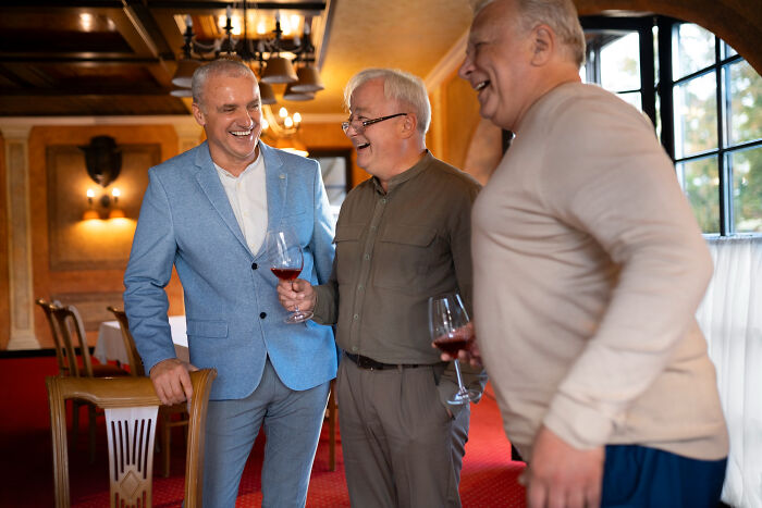Three men laughing and holding wine glasses in a warmly lit room, discussing common misconceptions about women.