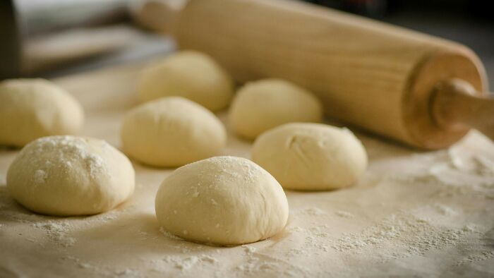 Uncooked dough balls on a floured surface with a wooden rolling pin, showing a common childhood baking activity.