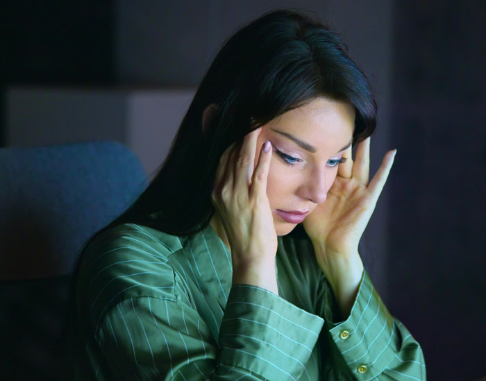 Woman in green shirt holding her head in worry, reflecting on experiences of people who lost a friend to tumour news.