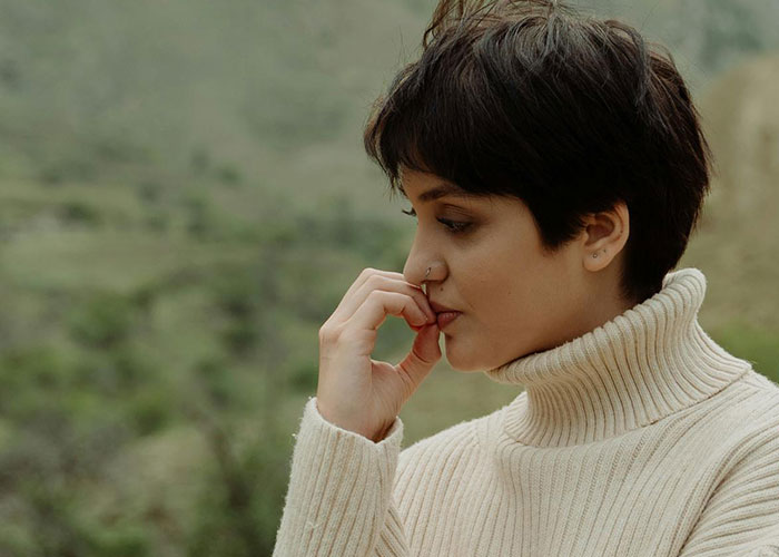 Young woman in a cream turtleneck sweater, deep in thought, reflecting on messy love triangle secrets outdoors.