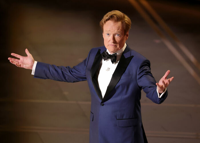 Conan O’Brien in a navy tuxedo gesturing on stage during Oscars 2026 monologue amid backlash over awkward joke. Conan O’Brien in a navy tuxedo gesturing on stage during Oscars 2026 monologue amid backlash over awkward joke.